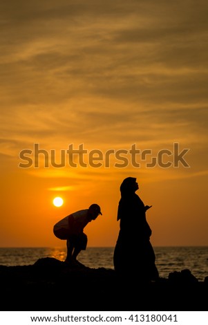 Silhouette Muslimah tourist couple taking photo before sunset on the beach rock , Phuket Thailand.