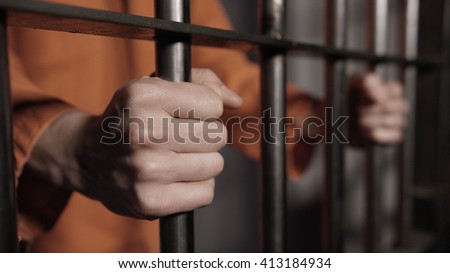 Caucasian man's hands on the bars of a prison cell Royalty-Free Stock Photo #413184934
