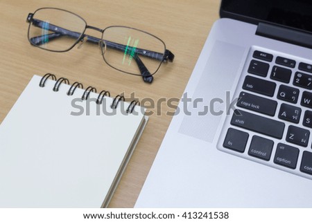 Still life, laptop, nodepad, eyeglasses on wooden table.