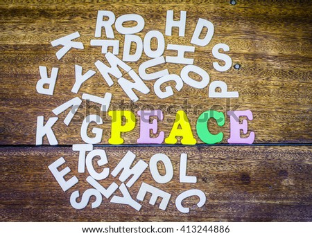 word " peace "design by colorful letterpress  surrounded by white letterpress on wooden background