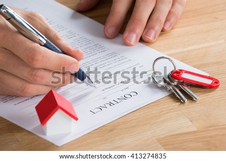Close-up Of Businessman Filling Contract Form With Key And House Model On Desk