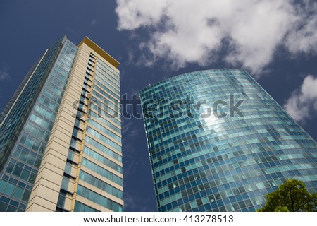 Two glass high office or hotel skyscraper building with one green fresh tree growing outdoor sunny weather with blue and white cloudy sky on natural background, horizontal picture