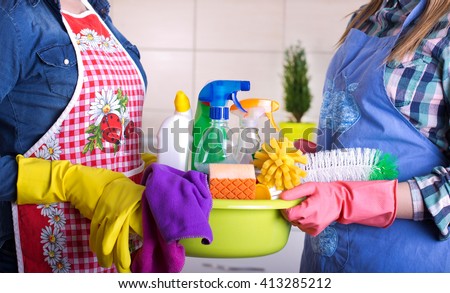 Two cleaning women holding basin full of cleaning supplies in the kitchen. House keeping and teamwork concept Royalty-Free Stock Photo #413285212