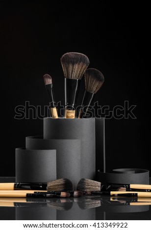 Make-up brushes in curls of matted carton in minimalistic style. Dark background. Reflecting surface of the table with objects' shadows. Creative still life. The grace of the black color.