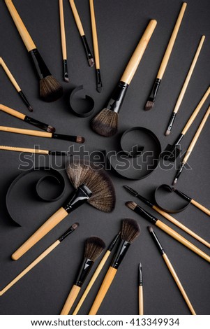 Usual contents of makeup bag of every professional make-up artist or active user of cosmetics. Huge assortment of various brushes for make-up. The picture with creative whorls on black table.