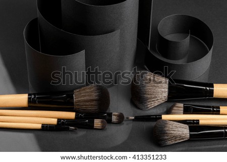 Make-up brushes and accurate curls of black matted carton. Unusual still life in minimalistic style. Objects of beauty industry in foreground.