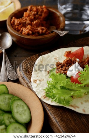 Closeup Mexican Tacos with ground beef and lettuce, tomato and cucumber on old cutting board