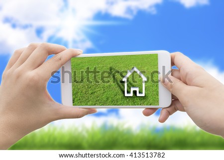 woman hand holding the phone with green grass and a house on the screen