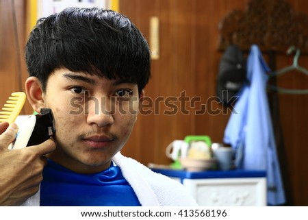 Handsome man sitting to cut hair   in THAILAND.
Handsome man with dark hair wearing white shirt doing a haircut for man with black hair at barber shop, copy space, close up.