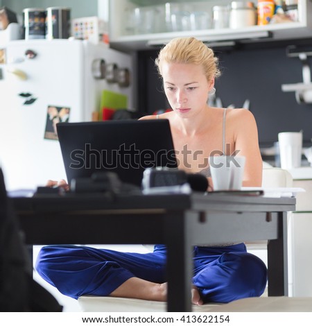 Female freelancer in her casual home clothing working remotly from her dining table in the morning. Home kitchen in the background.