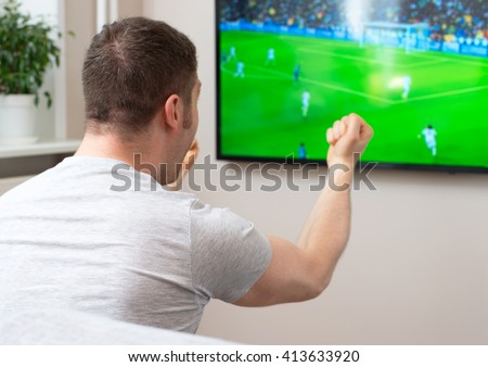 Goal! Man watching football match on television at home. Royalty-Free Stock Photo #413633920
