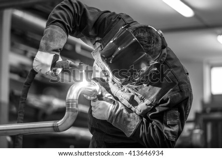 Industrial worker with protective mask welding inox elements in steel structures manufacture workshop. Black and white photo.