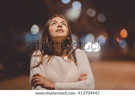 Portrait of beautiful young lady looking up, city street in the night, evening lights bokeh outdoors background 