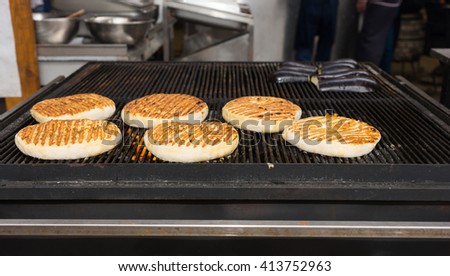 Buns for burgers grilling over a fire in a commercial kitchen ready for serving with hamburgers, low angle view