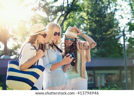 Three attractive girls looking at photos on their camera at summer holidays, girl friends on their travel vacation