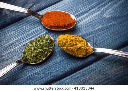 Colorful spices on silver spoons placed on blue grunge wooden table.