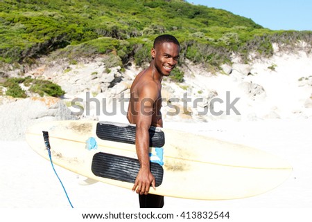 Portrait of smiling young african man at beach with surfboard