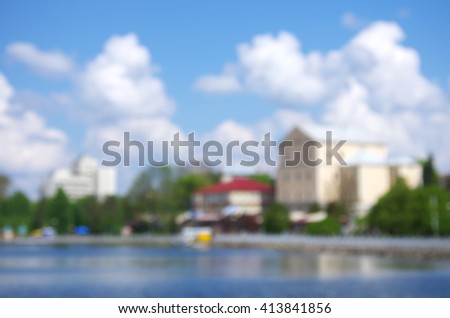 a blurred cityscape with lake in the foreground and the white clouds in blue sky in the background