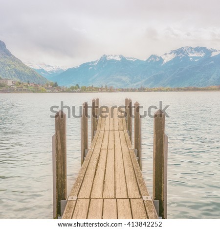 A wooden pier in lake Geneva, Montreux, Switzerland. A view from Chateau de Chillon (Chillion castle) with snow moutain in background. A picture with retro filter.