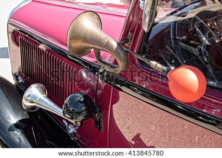 Close up view of two shiny metal horns on red classic car. Sound signal used to avoid traffic accidents. Way of warning or informing people about danger. Royalty-Free Stock Photo #413845780