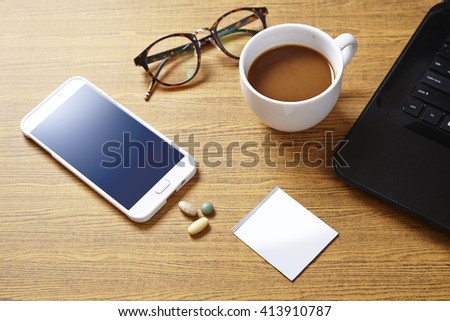 Wooden desk with a computer, coffee cup,cellphone and some pills ,working and health concept.