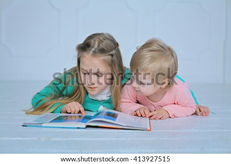education and school concept - little sisters lying on a floor with a book studying and reading. happy kids boys brothers reading encyclopedia together at home