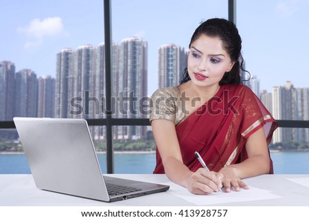 Picture of Indian young businesswoman working in the office while wearing sari clothes and using laptop