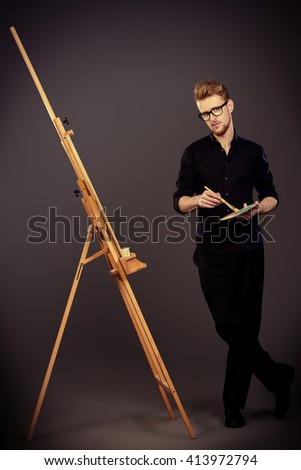 Male artist paints on an easel in the workshop. Occupation.