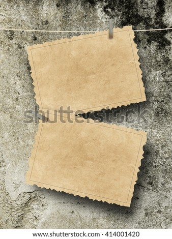 Close-up of two blank old postcard frames hanged by pegs against brown weathered wall background