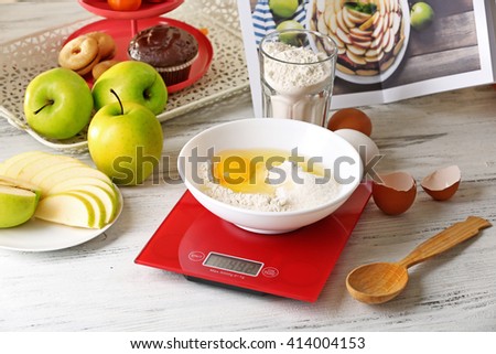 Bowl of raw egg and flour with digital kitchen scales on light wooden table