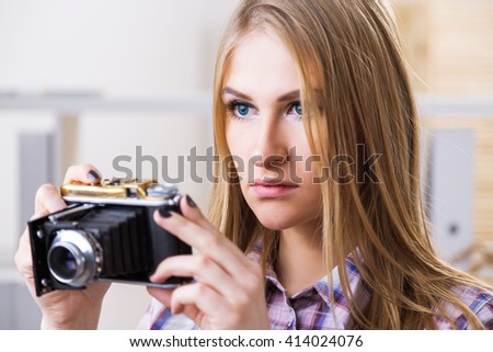 Attractive female about to take a picture with a retro camera on blurry background