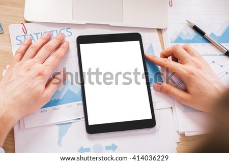 Hands with blank white tablet on wooden desktop with business report on paper sheets. Topview, Mock up