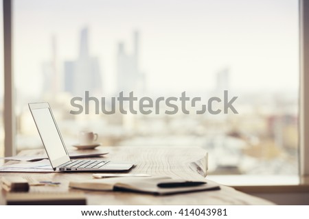 Sideview of office desktop with blank laptop and various office tools on blurry Moscow city background