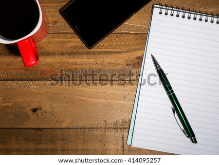 Pen, paper and a coffe mug on a wooden table.