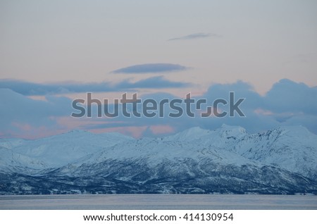 majestic snowy mountain with colorful sunset sky and beautiful cloud formation with cold fjord water underneath in wintertime