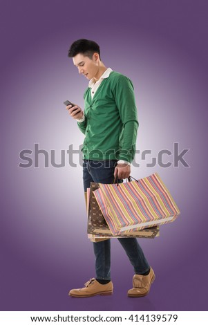 Asian young man holding shopping bags and using cellphone, full length portrait isolated.