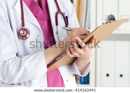 Close up view of female doctor hands holding clipping pad and filling patient history or prescribing some medicines. Healthcare and medical concept.