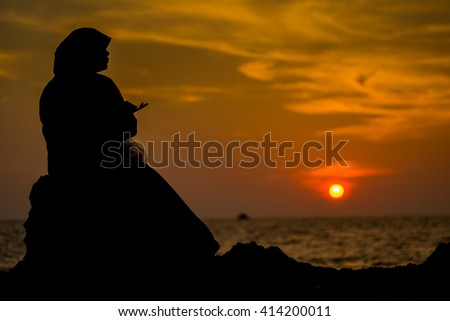 Silhouette Muslimah woman tourist texting on smartphone before sunset on the beach rock , Phuket Thailand.