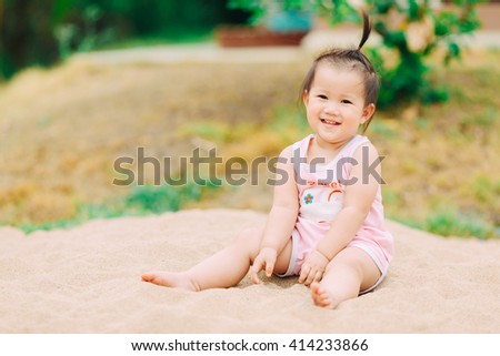 an 1 year old baby playing in the sands. This activity is good for sensory experience and learning by touch their fingers and toes through sand and enjoying its texture.  Soft focus picture style.