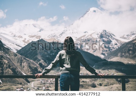 Young beautiful woman enjoys mountain view from a terrace. Freedom concept. Travel and tourism. Toned picture