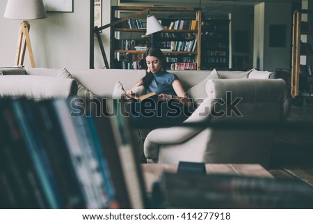 Young beautiful woman enjoys reading sitting on a comfortable couch. Learning and knowledge concept. Toned picture