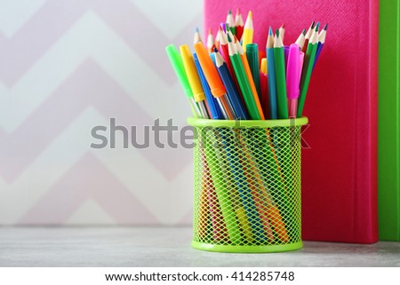 Books pens and markers in metal holder on colour background