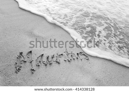Mauritius written in the sand and about to be erased by a wave. Black and white closeup picture of inscription on the sand