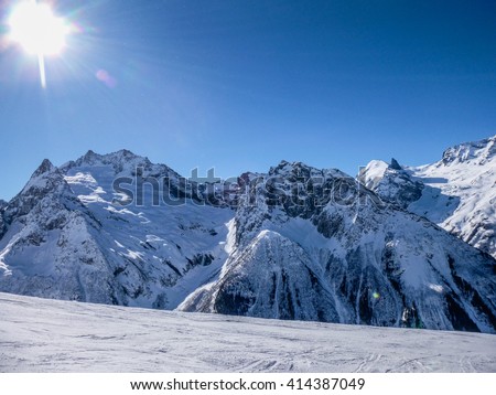 Snowy mountains with the slope for snowboarders and skiers on the blue sky with sun background