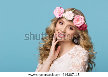 Beauty portrait. Beautiful blonde woman with wreath of flowers. Looking at camera. Touching hair. Isolated on blue background. Youth, happiness concept Royalty-Free Stock Photo #414387115