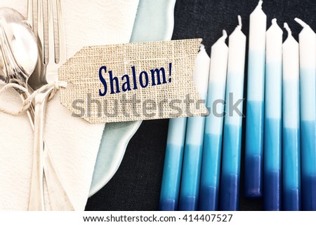 Above Closeup of Hanukkah Table Place Setting with Candles, Plates, Silverware, Napkin and Shalom Name Tag and Room or Space for your words, text or copy over blur candles. Horizontal bleach by-pass