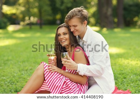 Young beautiful caucasian couple hugging and drinking wine at picnic in summer park on green grass