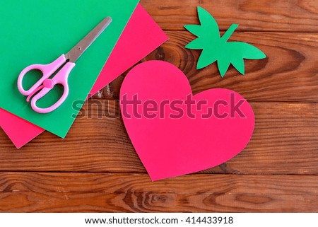 Paper red heart, paper green leaves on a wooden table. Paper pattern. Paper sheets, scissors - set for children's art. Kids crafts. DIY concept. 