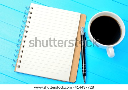 Notebook with cup of coffee and pen on blue wooden table