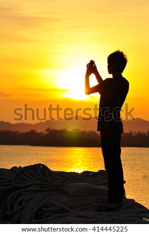 A silhouette of man taking photos of sunset with mobile phone with the background of orange sunset. stock photo . copy space